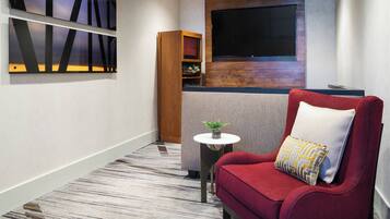 A modern hotel room with a red sofa, a small round table with a plant, and abstract wall art.