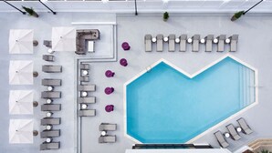 An aerial view of a rooftop pool area with a heart-shaped pool, sun loungers, and umbrellas.