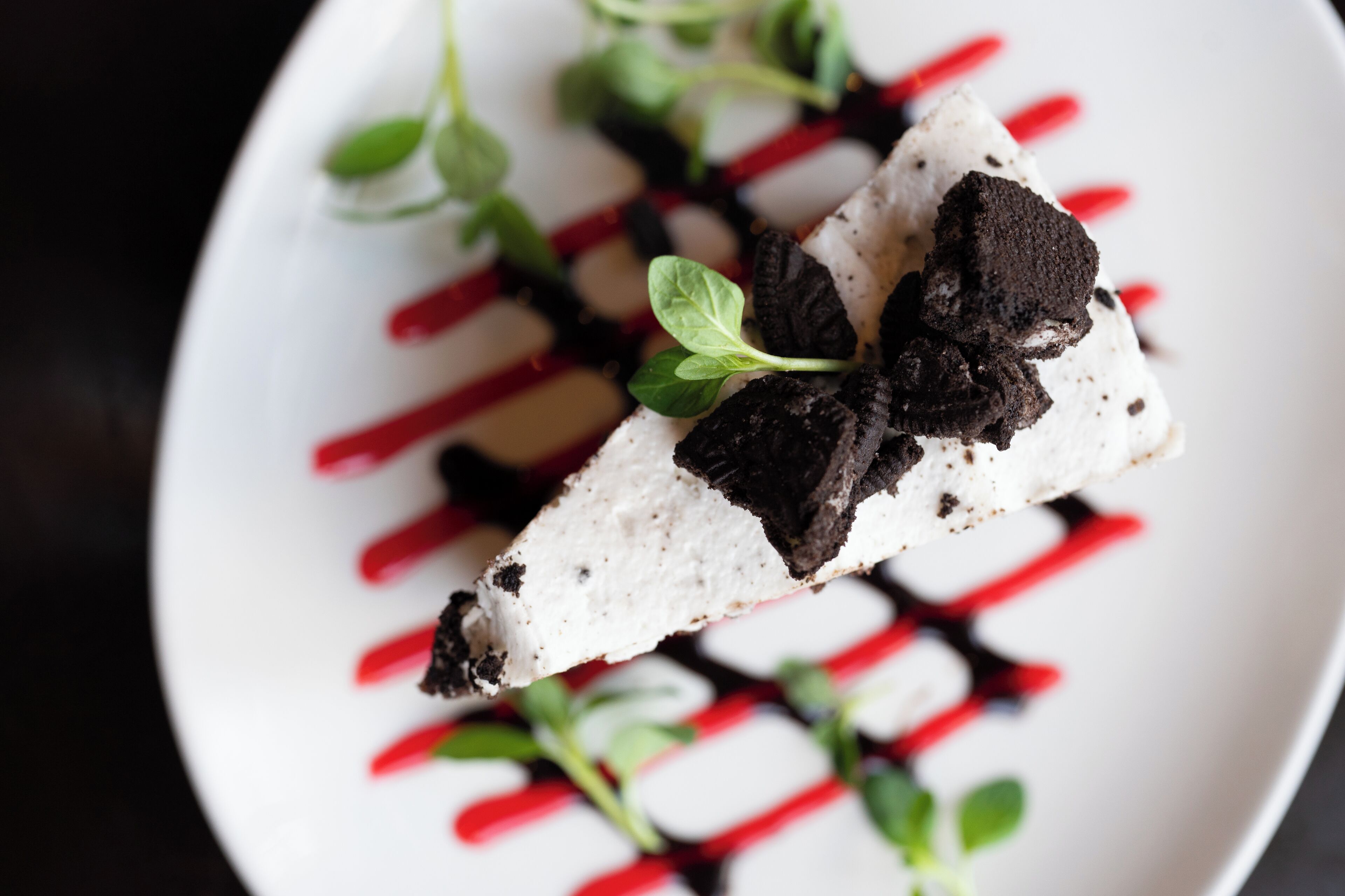 Un postre con trozos de chocolate blanco y negro, adornado con hojas verdes, sobre un plato blanco con líneas rojas.