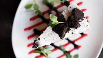 Un postre con trozos de chocolate blanco y negro, adornado con hojas verdes, sobre un plato blanco con líneas rojas.