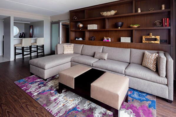 A modern living room with a sectional sofa, ottomans, a coffee table, and a bookshelf.
