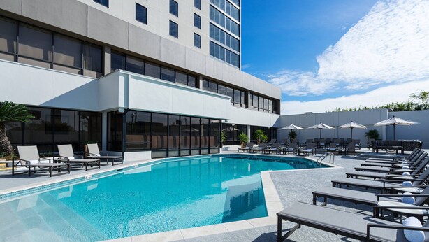 A modern hotel with a swimming pool, sun loungers, and umbrellas.