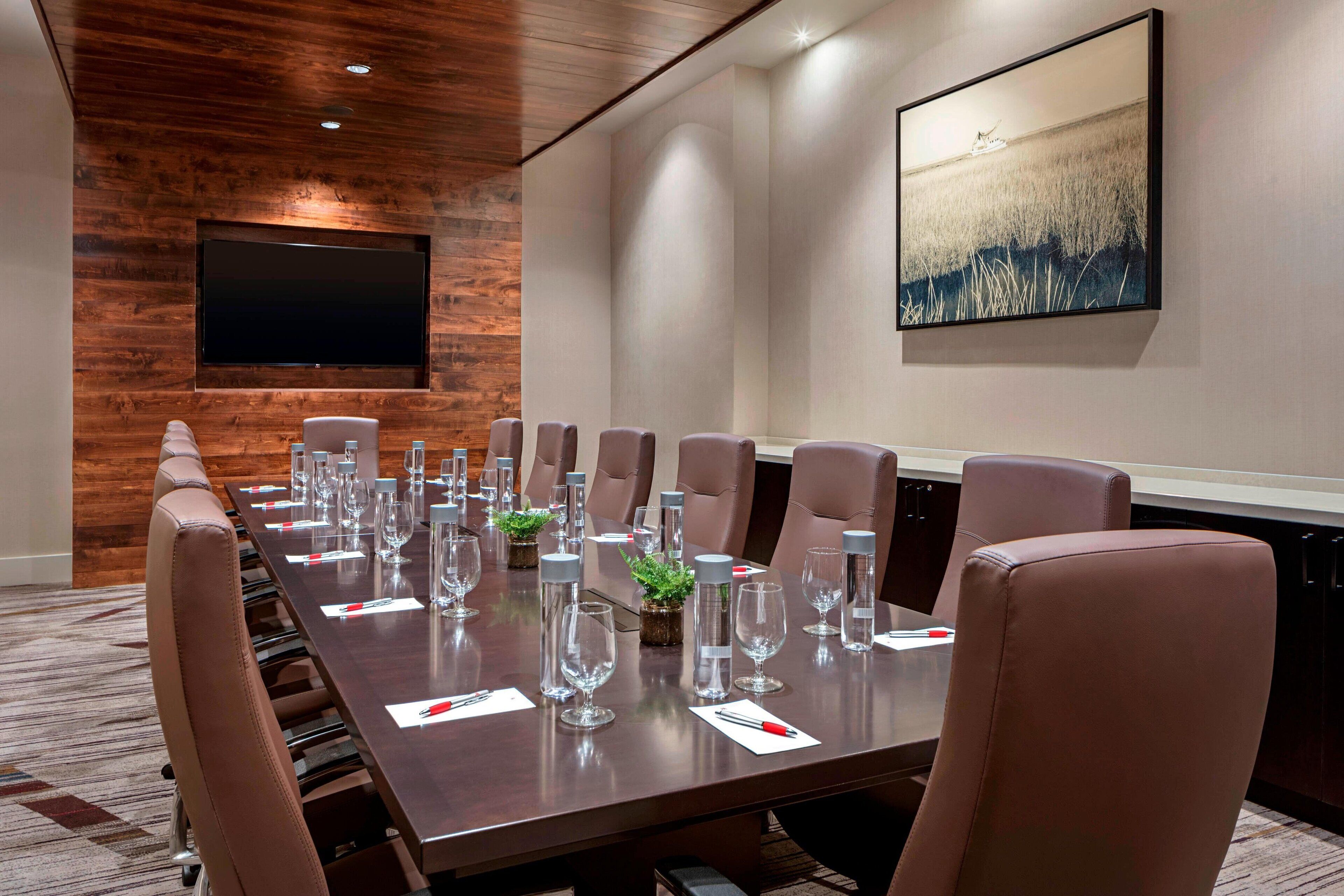 A conference room with a long table, brown leather chairs, and a flat-screen TV mounted on the wall.