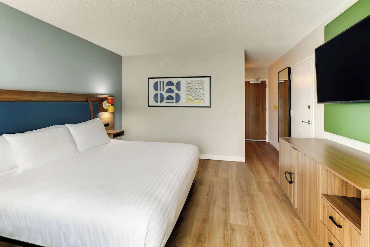 Een hotelkamer met een groot bed, houten vloeren, een flatscreen televisie, een kunstwerk in een lijst aan de muur en een houten kast.