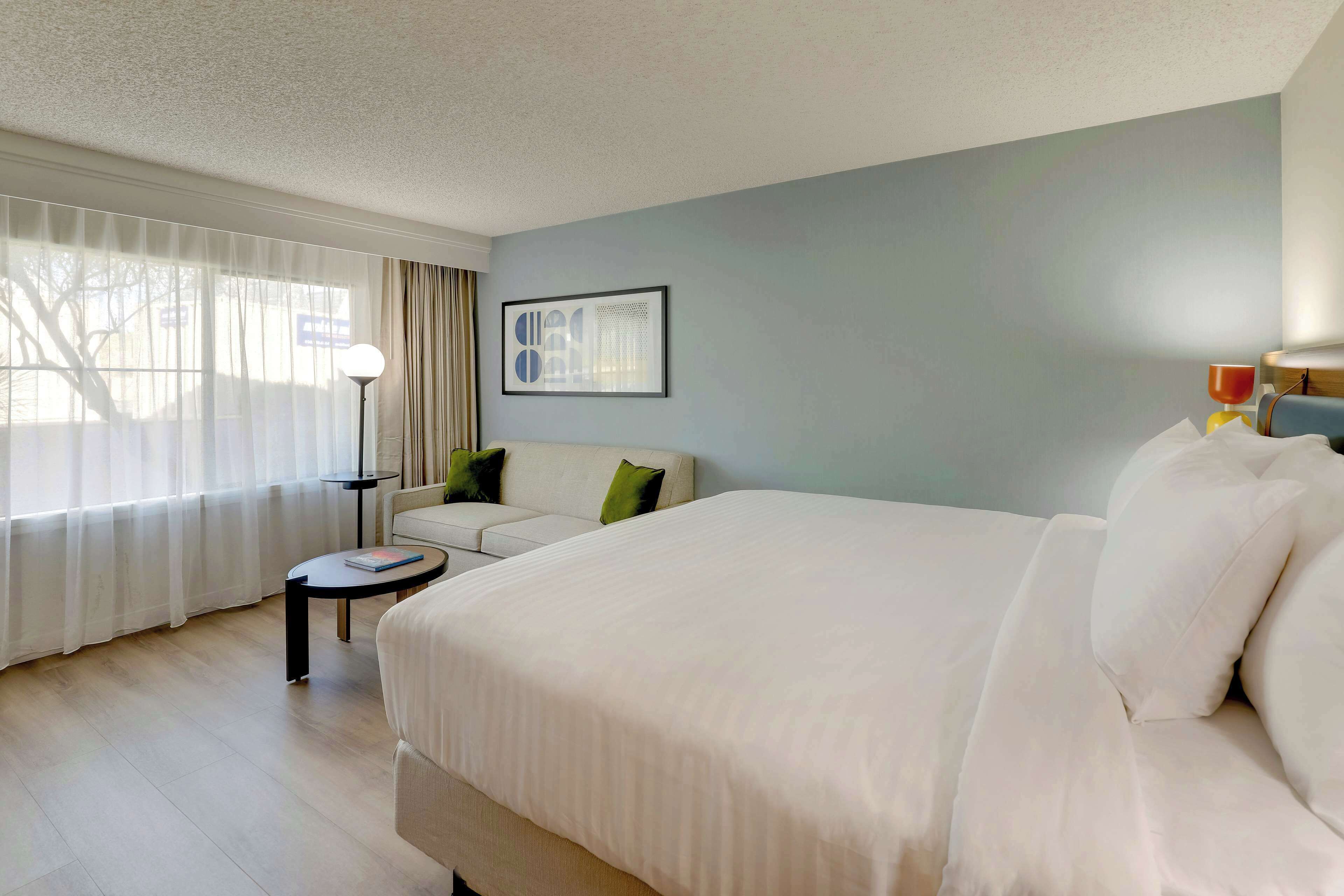 A hotel room with a large bed, a sofa, a small table, and a lamp.