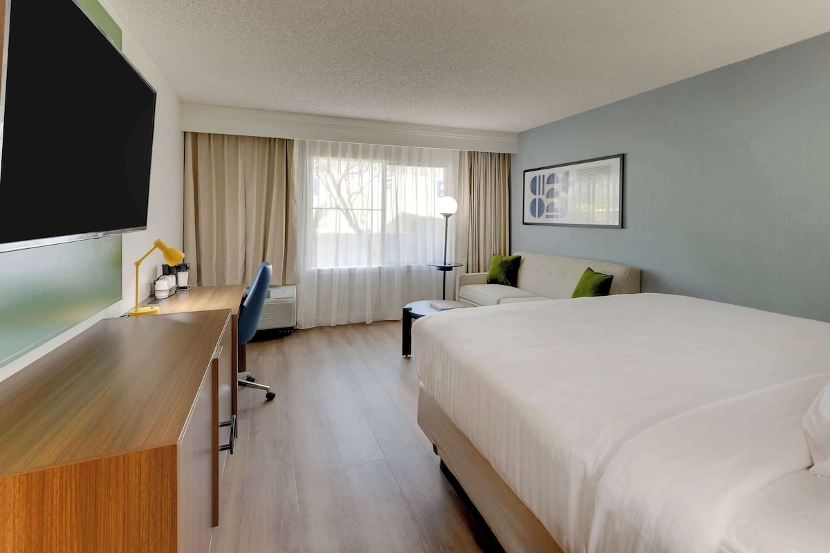 Een hotelkamer met een bed, een bureau, een stoel, een televisie en een raam met gordijnen.
