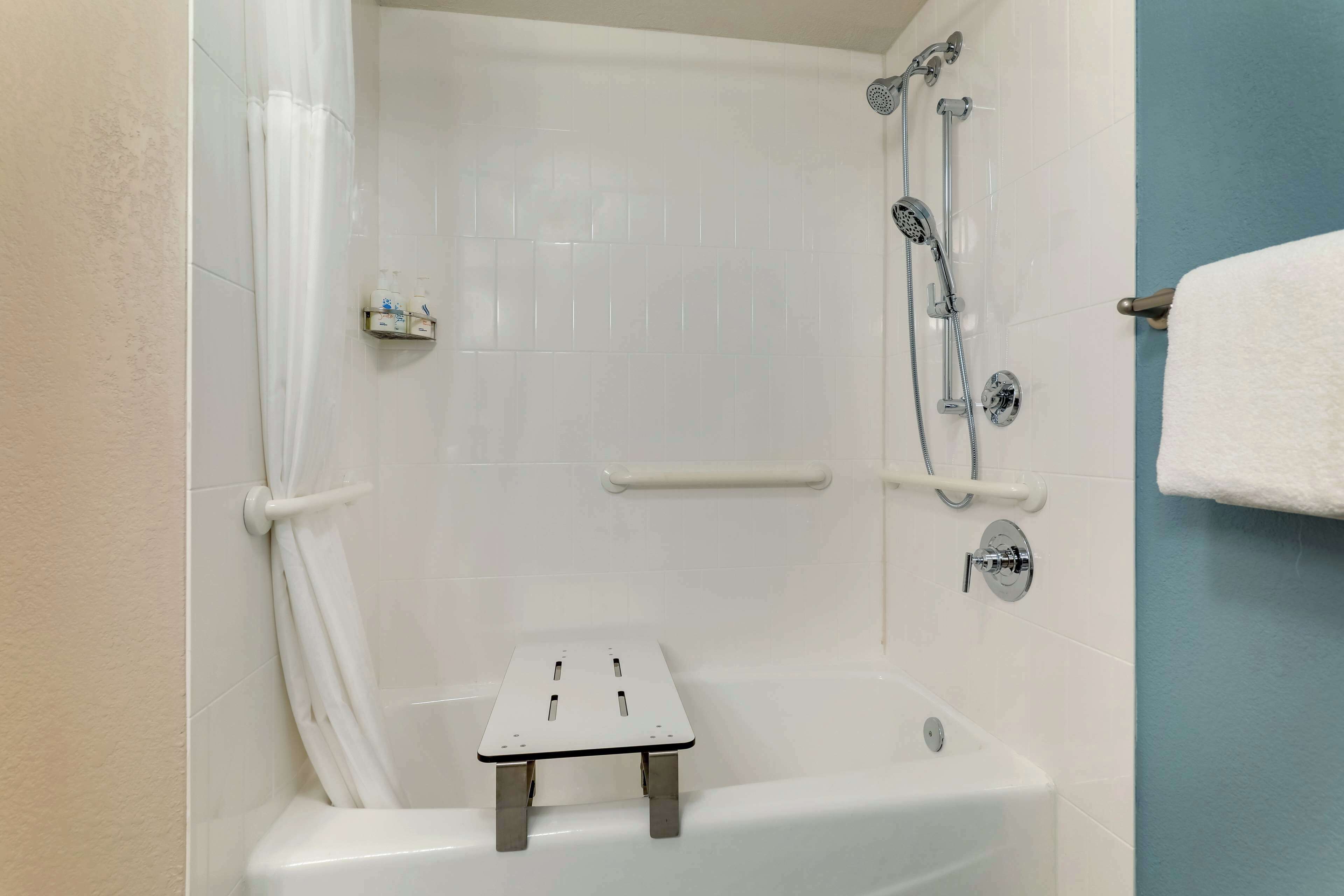 Een badkamer met een douche, een wit bad en een klein opstapkrukje, evenals een handdoekrek.