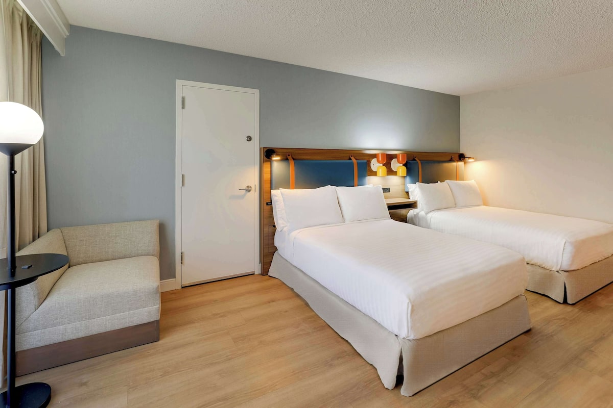 Een hotelkamer met twee bedden, een bank, een lamp en een deur.