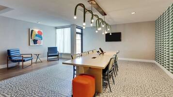 A conference room with a long table, chairs, a small orange ottoman, a painting on the wall, and a patterned floor.