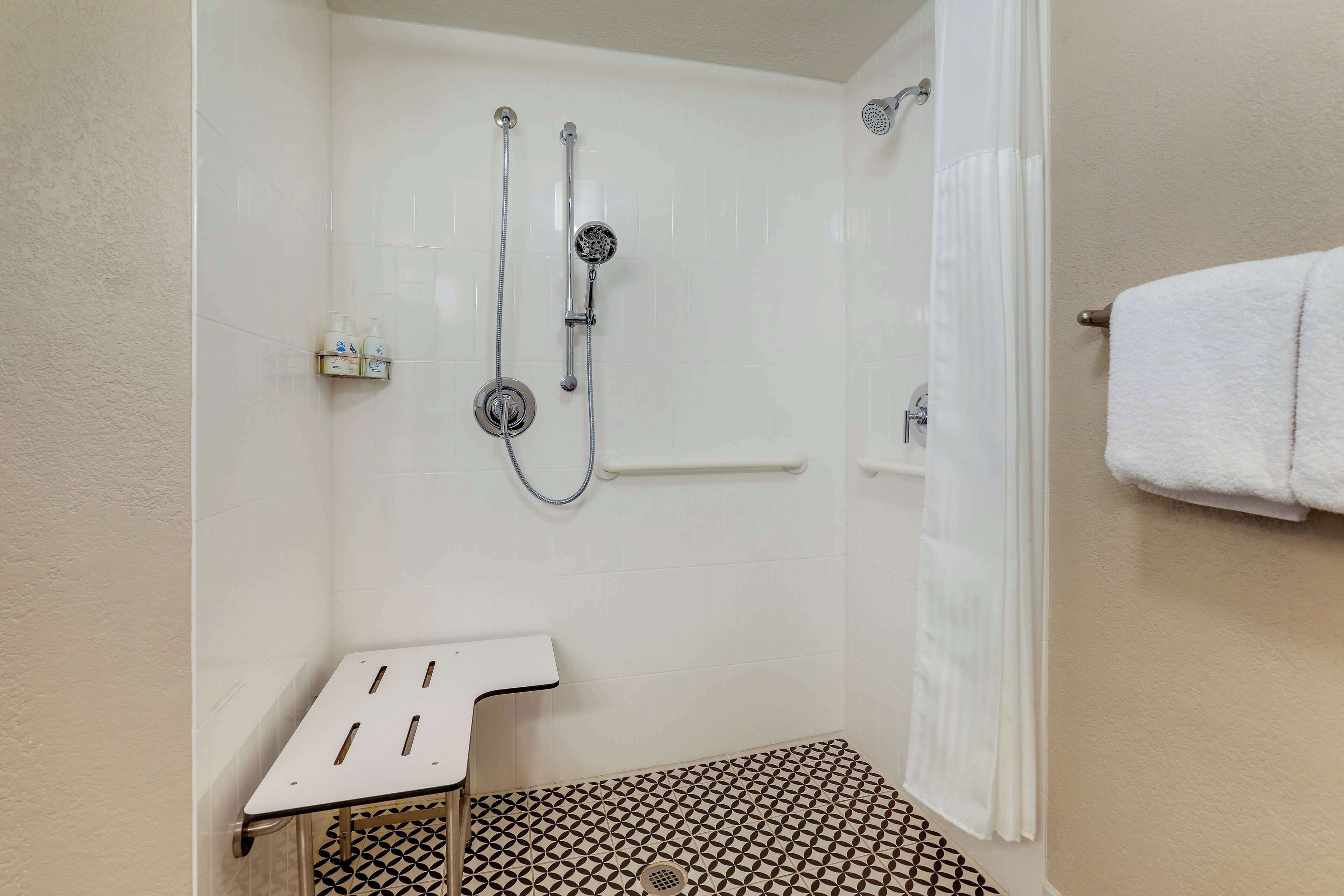 A shower area with a white tiled wall, a showerhead, a handheld shower attachment, and a towel rack.