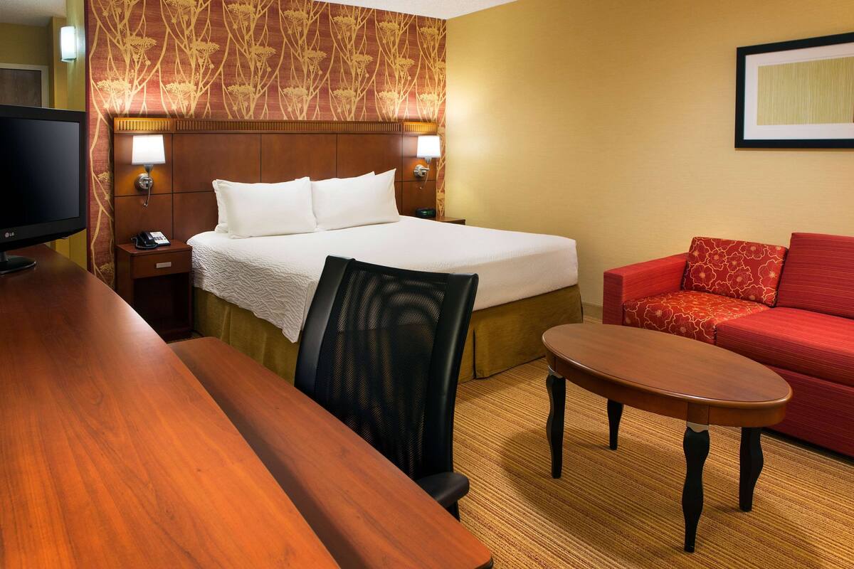 Een hotelkamer met een bed, een bureau, een stoel, een rode bank en een televisie.