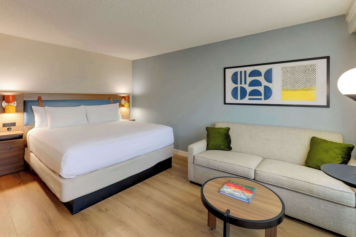 Een hotelkamer met een bed, een bank, een bijzettafeltje en een kunstwerk aan de muur.