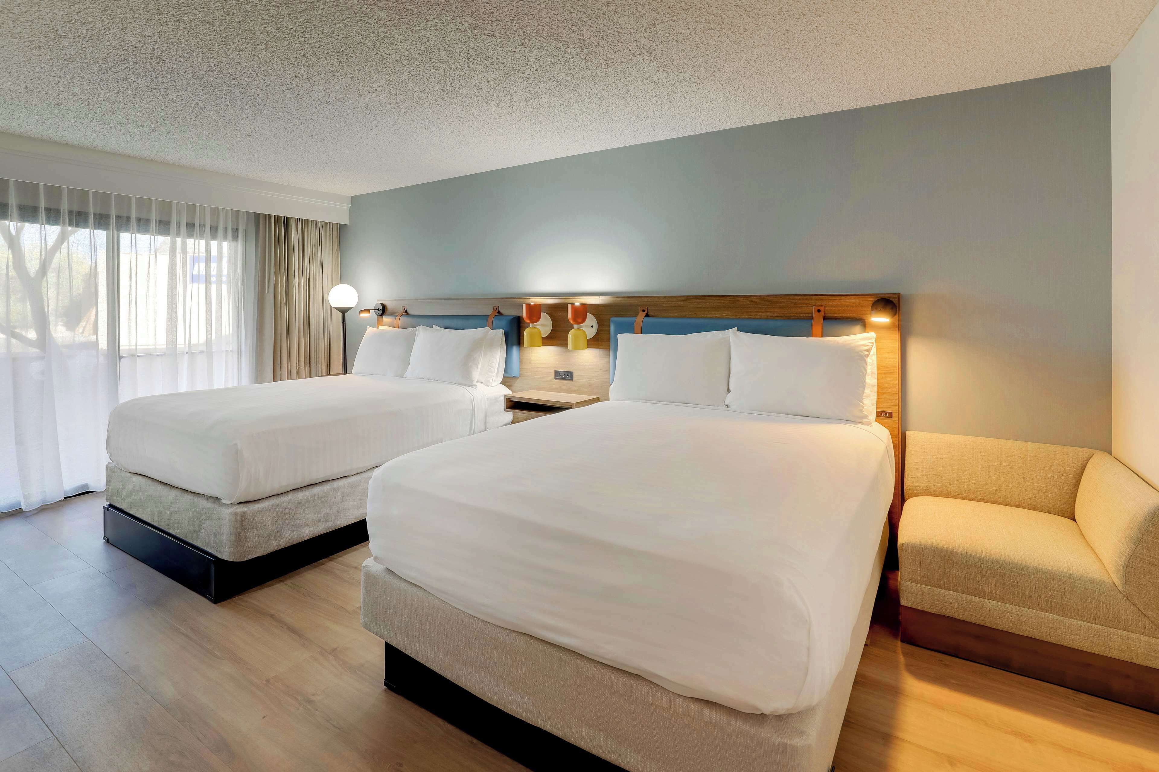 Una habitación de hotel con dos camas, un sofá y una mesita de noche con lámparas.