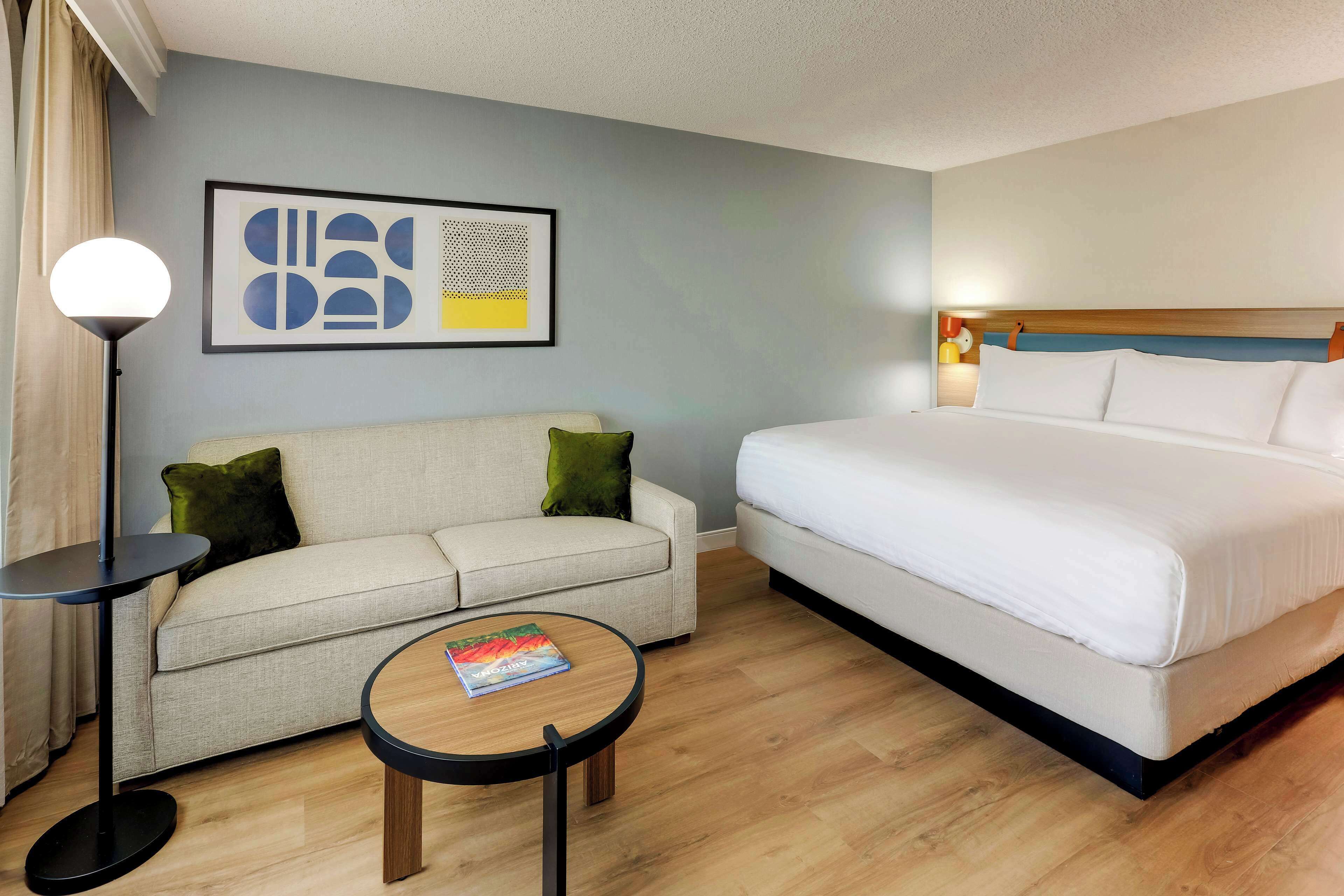 Una habitación de hotel con una cama, un sofá, una mesa de centro y una lámpara de pie.