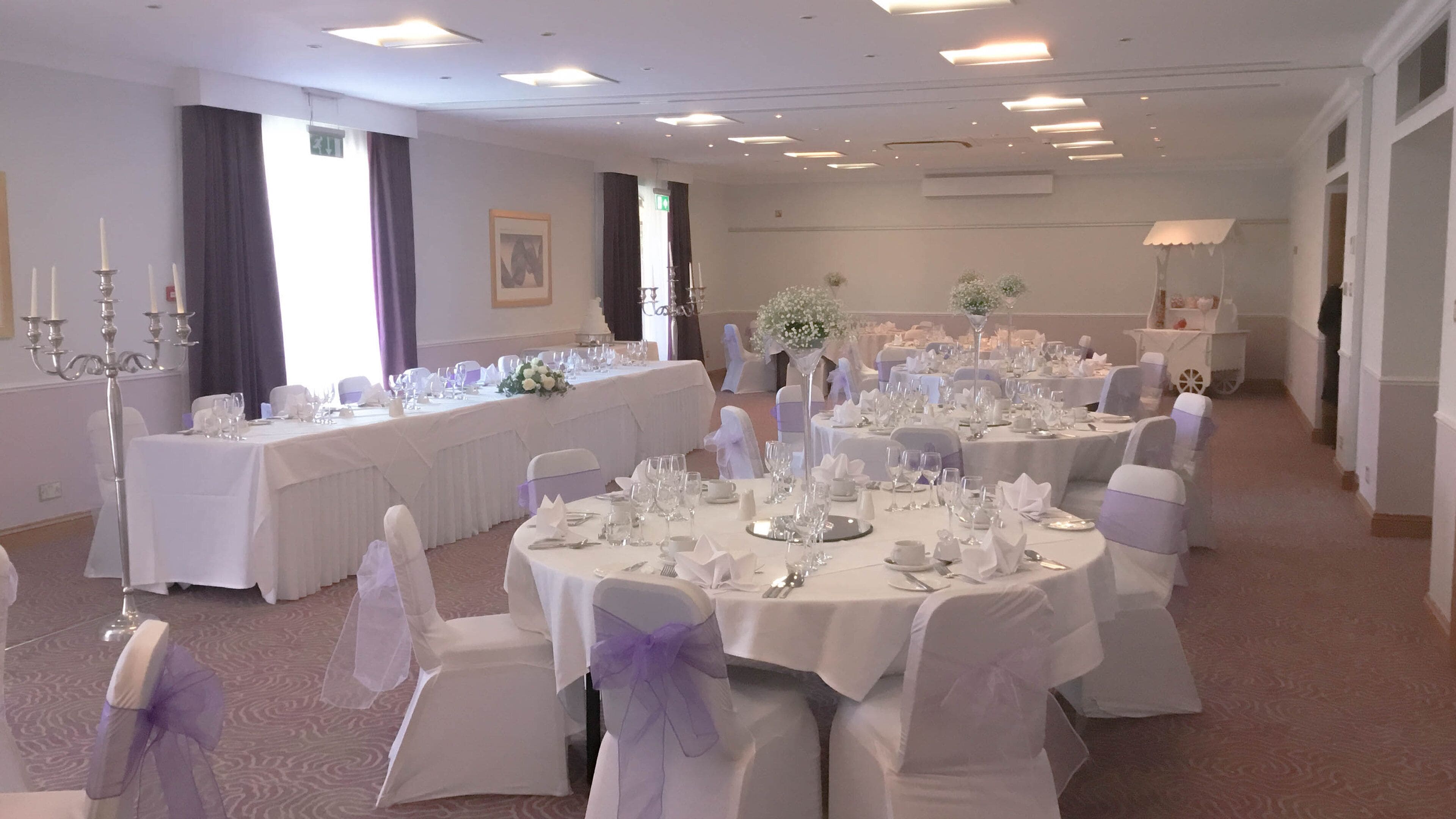 A banquet hall with round tables set for a formal event, featuring white tablecloths, silverware, and glassware.