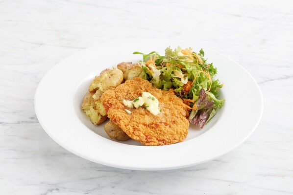 A plate with a breaded cutlet, potatoes, and a salad.