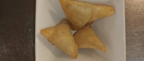 A square white plate with three triangular pastries on a dark surface.