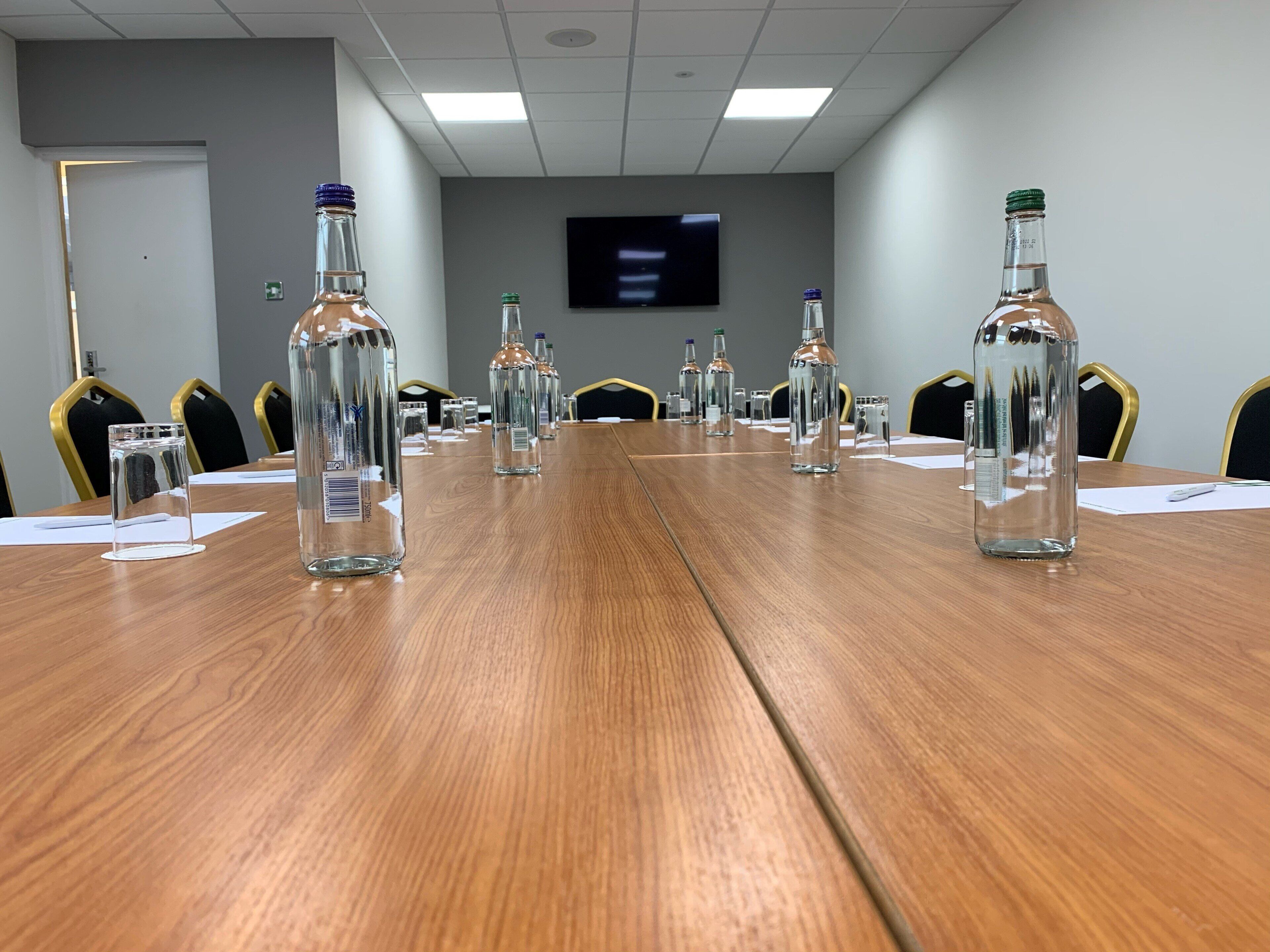 A conference room with a long wooden table, clear glass bottles, and chairs.