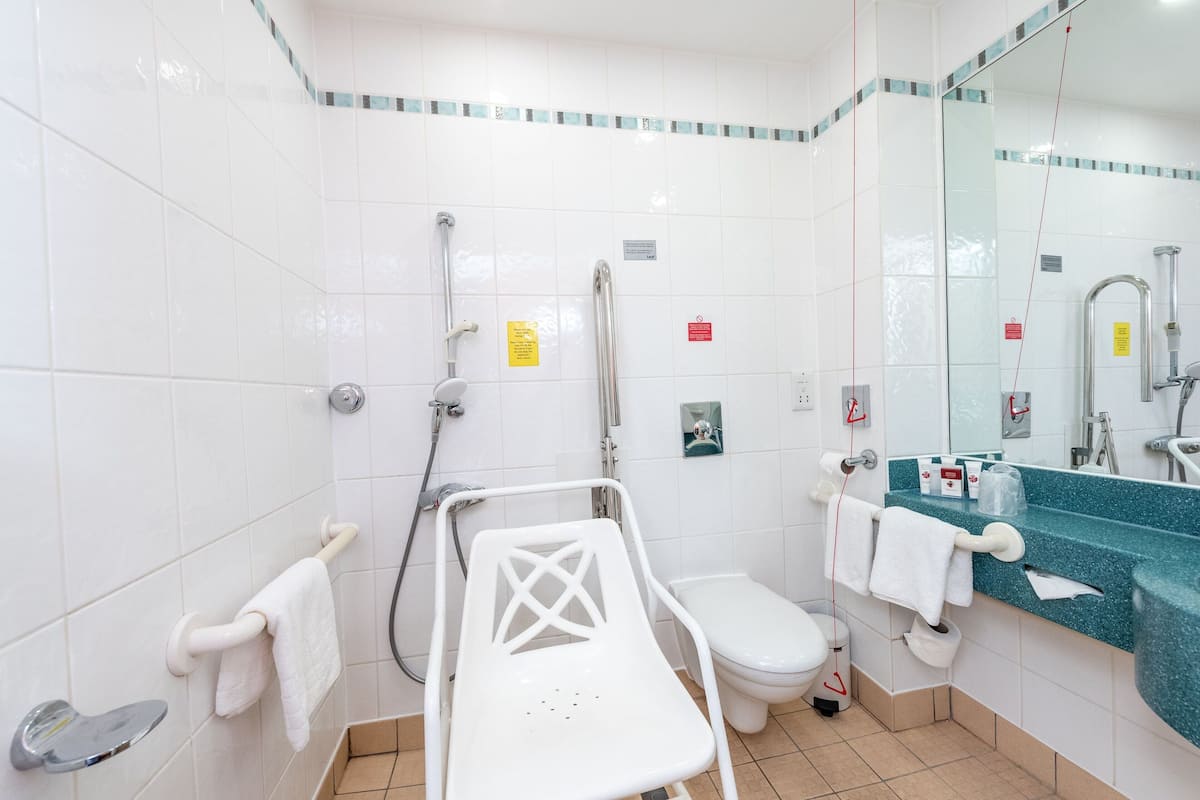 A bathroom with a white tiled floor, a white toilet, a shower area with a glass enclosure, a white sink with a blue countertop, and a white chair.