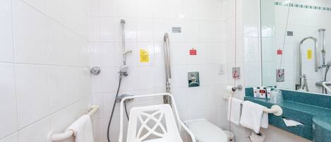 A bathroom with a white tiled floor, a white toilet, a shower area with a glass enclosure, a white sink with a blue countertop, and a white chair.