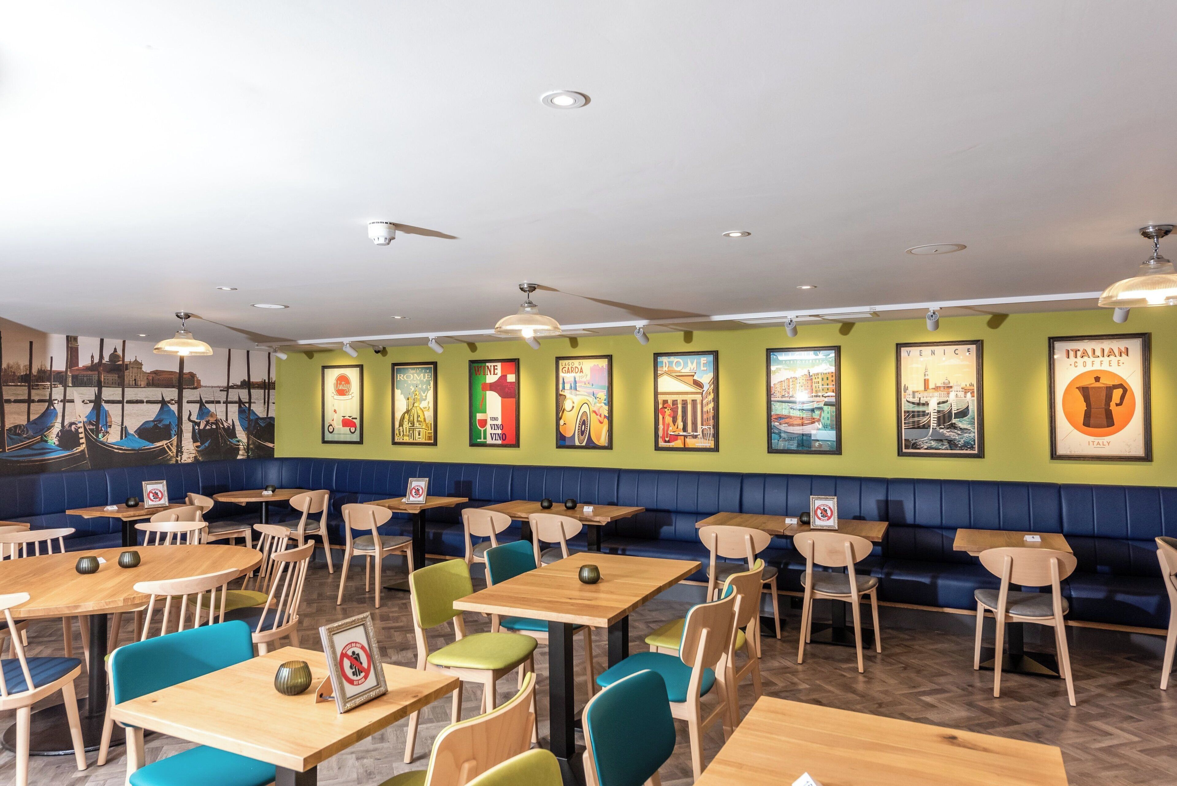 A restaurant interior with booths and tables, green walls, and travel-themed posters.