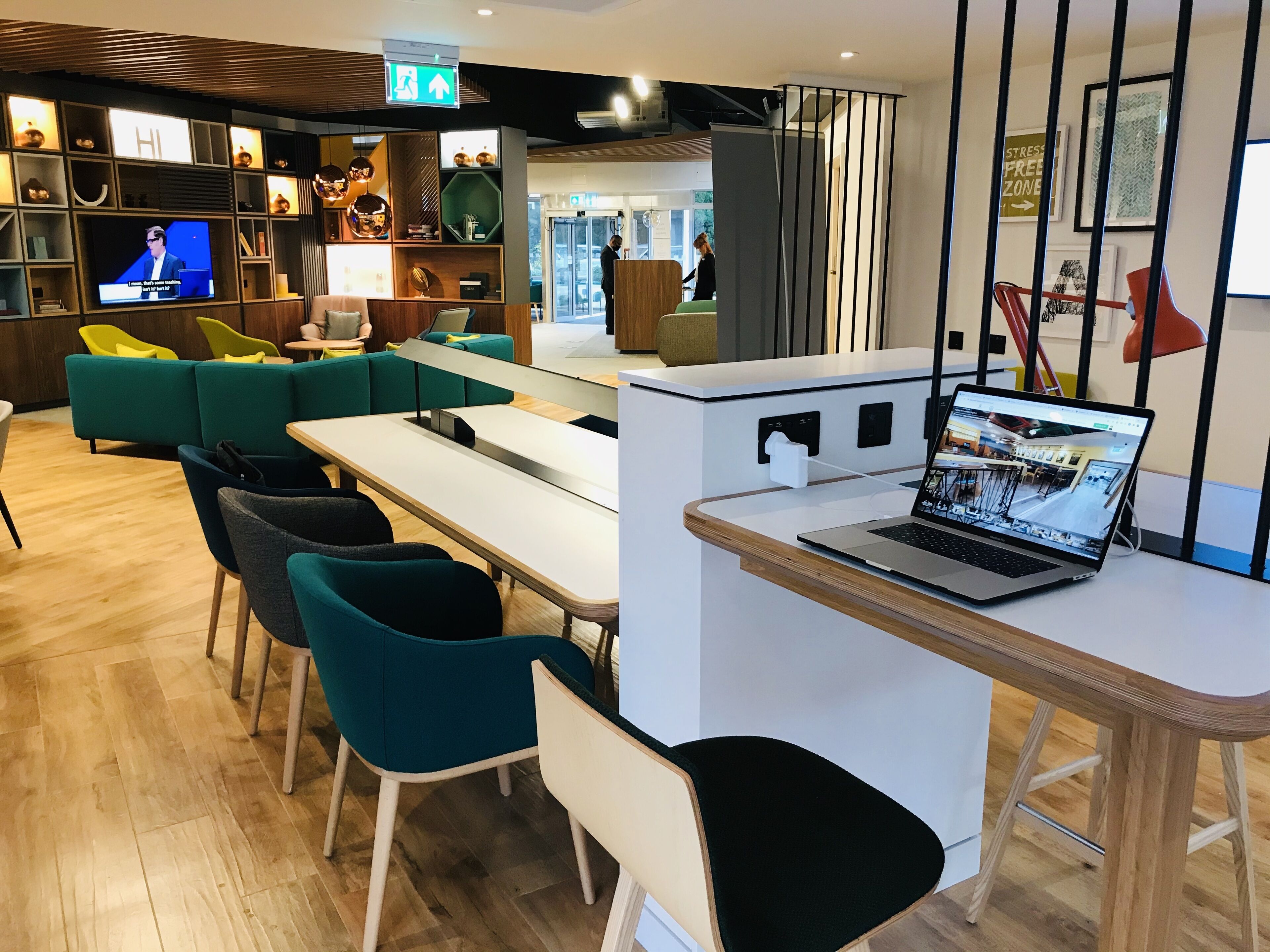Un área de descanso moderna con sillones azul verdoso y negros, una mesa blanca y una computadora portátil sobre un escritorio.