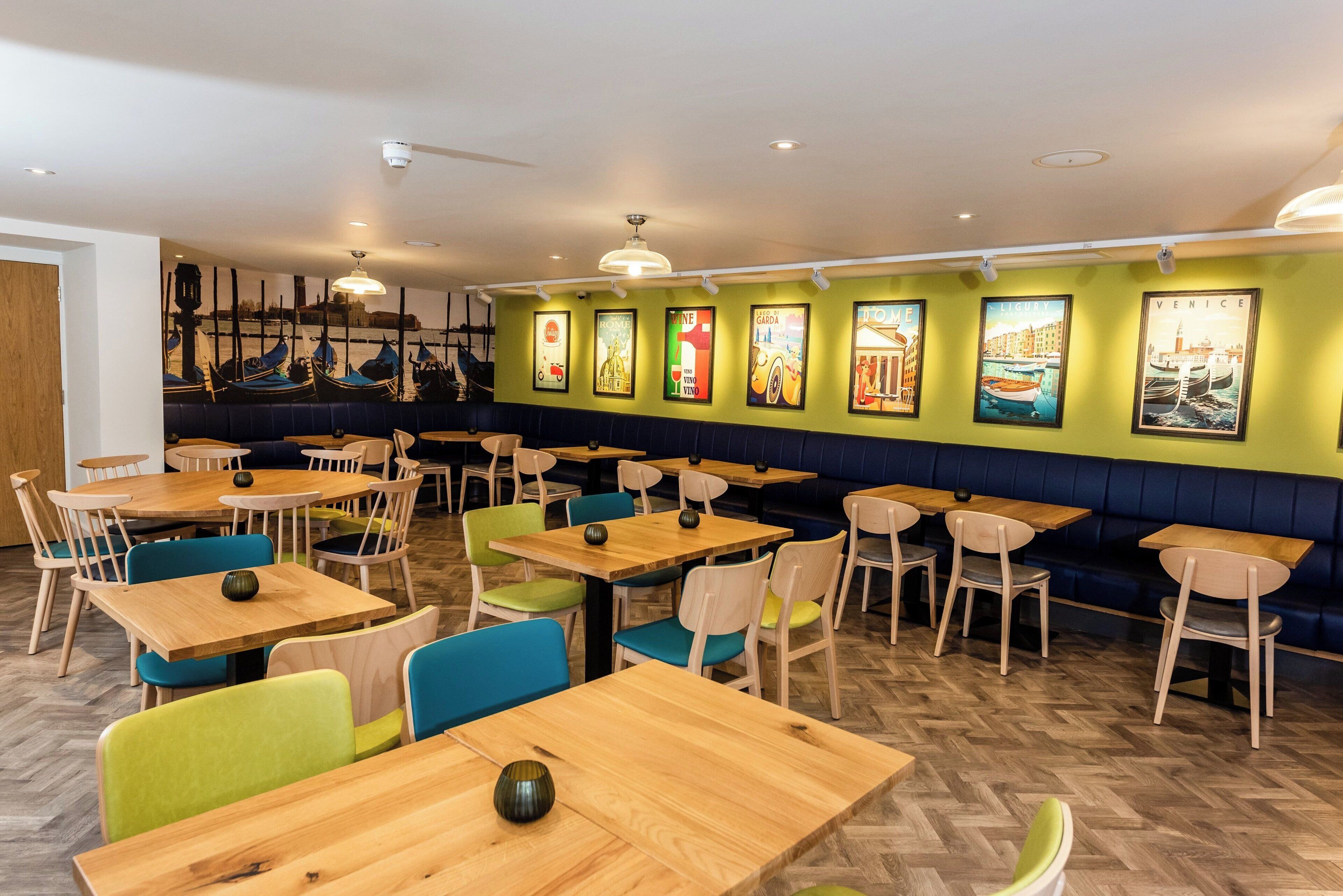 A restaurant interior with multiple tables and booths, wooden flooring, and wall-mounted artwork.