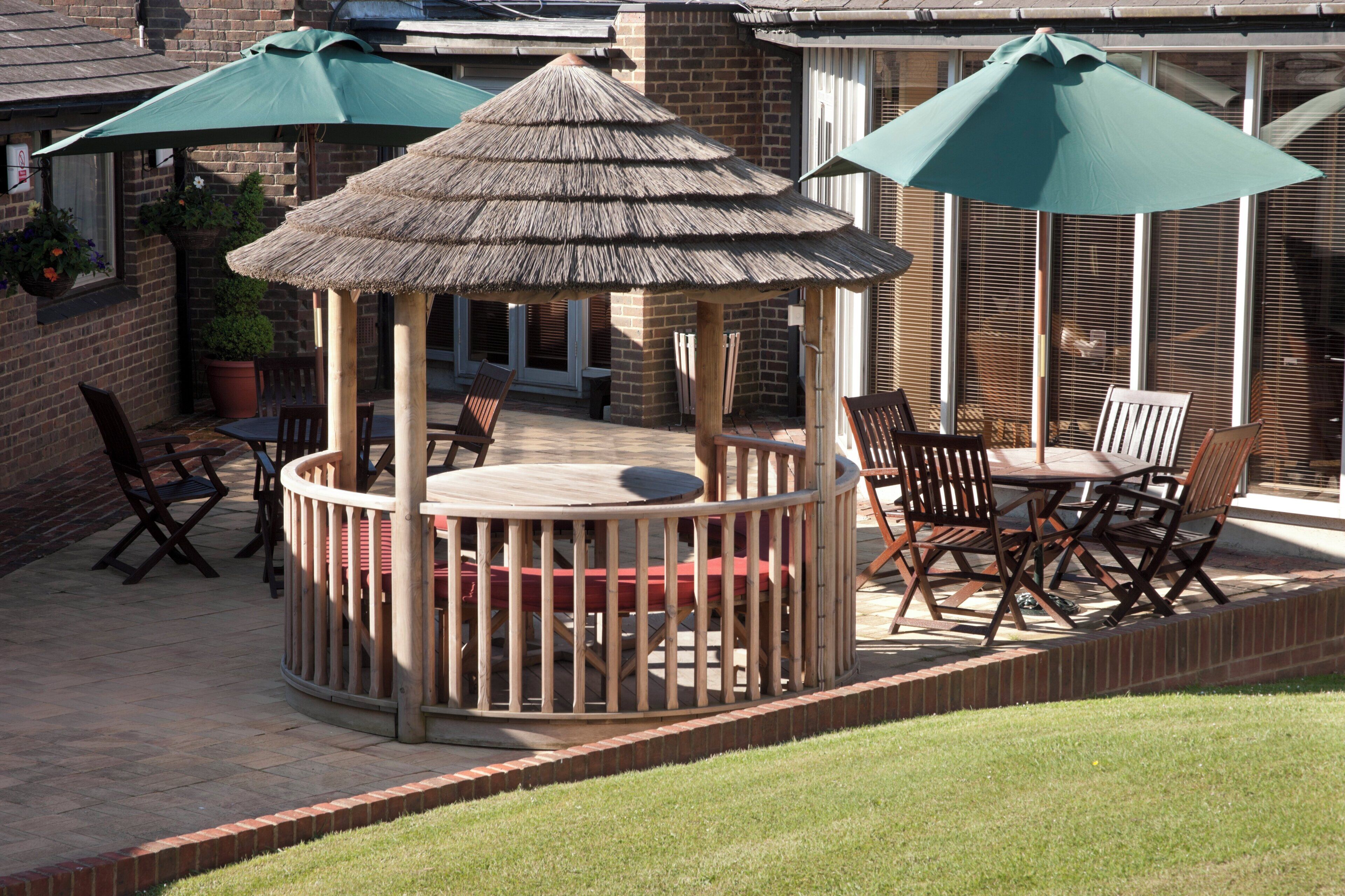 A wooden gazebo with a thatched roof, surrounded by outdoor furniture and potted plants.