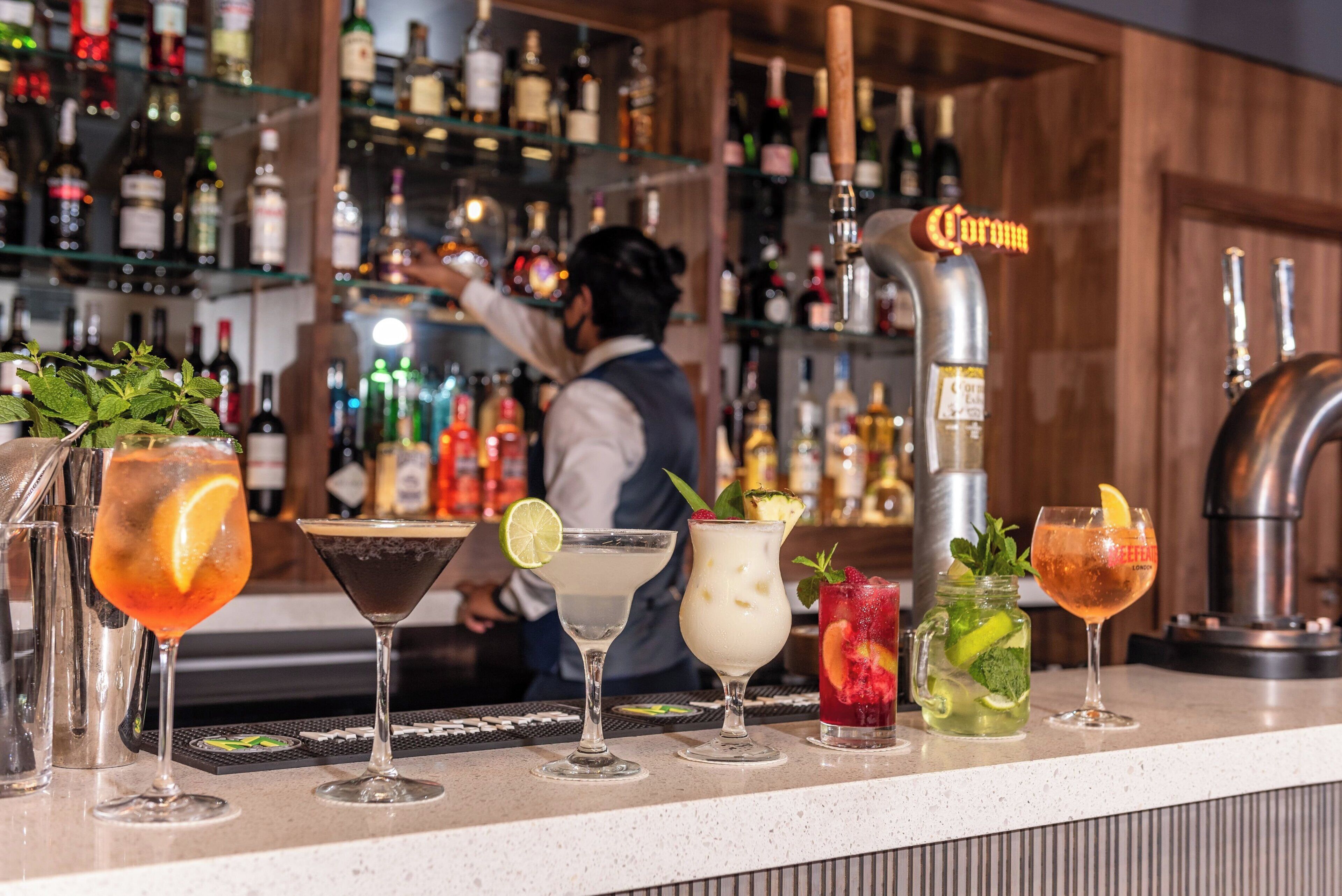 Un bar con varios cócteles y un barman preparando bebidas.