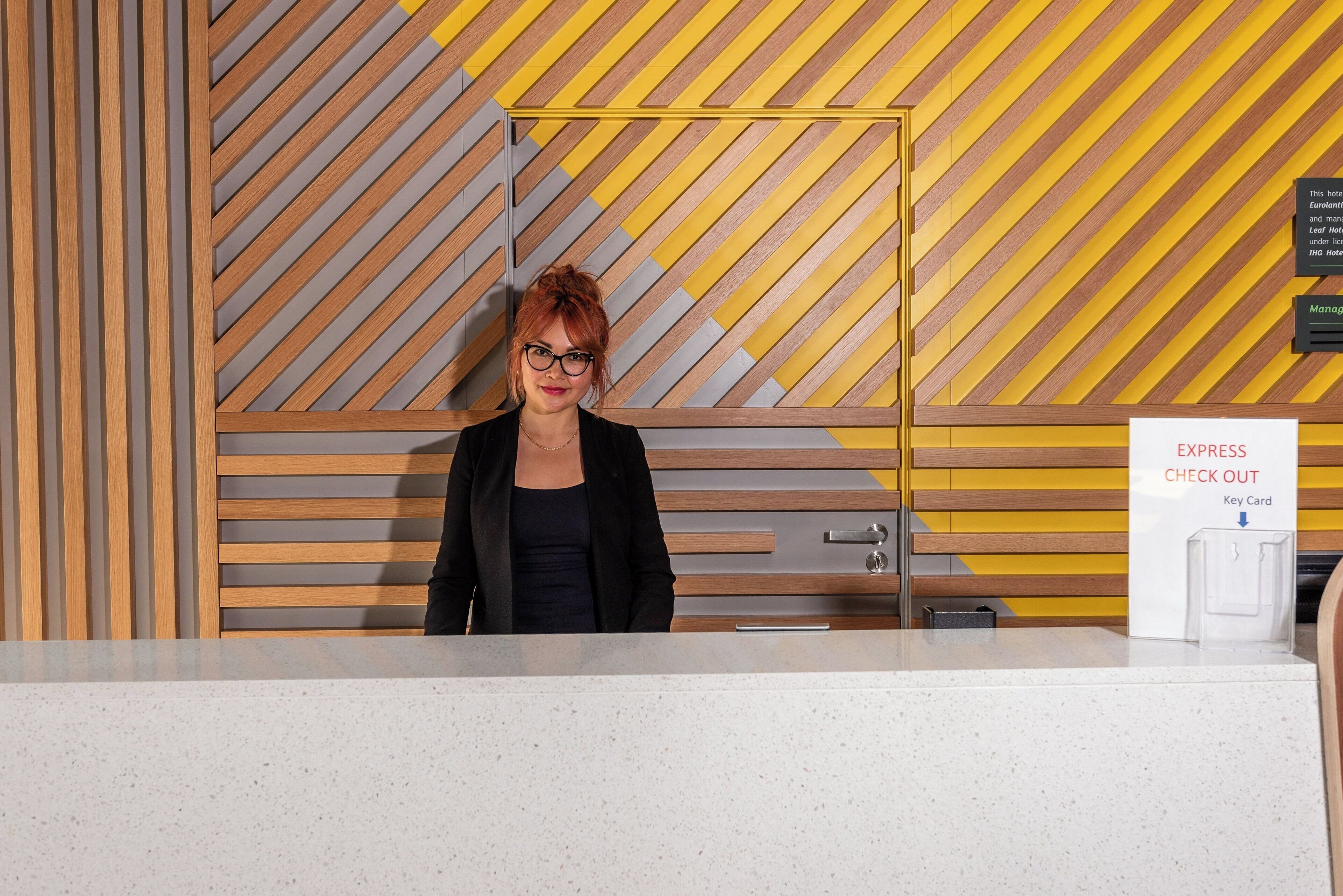 Un comptoir d’accueil d’hôtel au design moderne, comprenant un guichet pour l’enregistrement et un panneau indiquant la disponibilité d’un service d’enregistrement rapide.