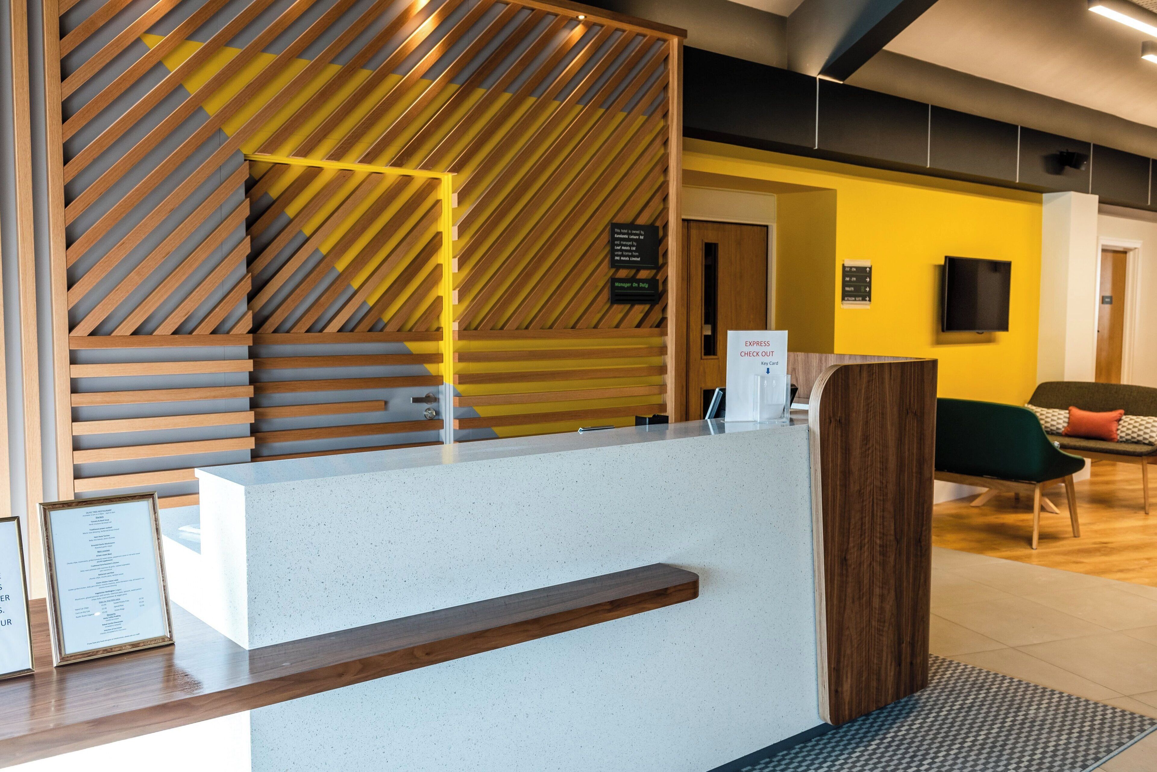 Ein Hotelrezeptionstresen mit modernem Design, inklusive einer Wand aus Holzlamellen und einer weißen Theke.