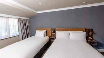 Habitación de hotel con dos camas, una mesita de noche con lámpara y una ventana con cortinas.