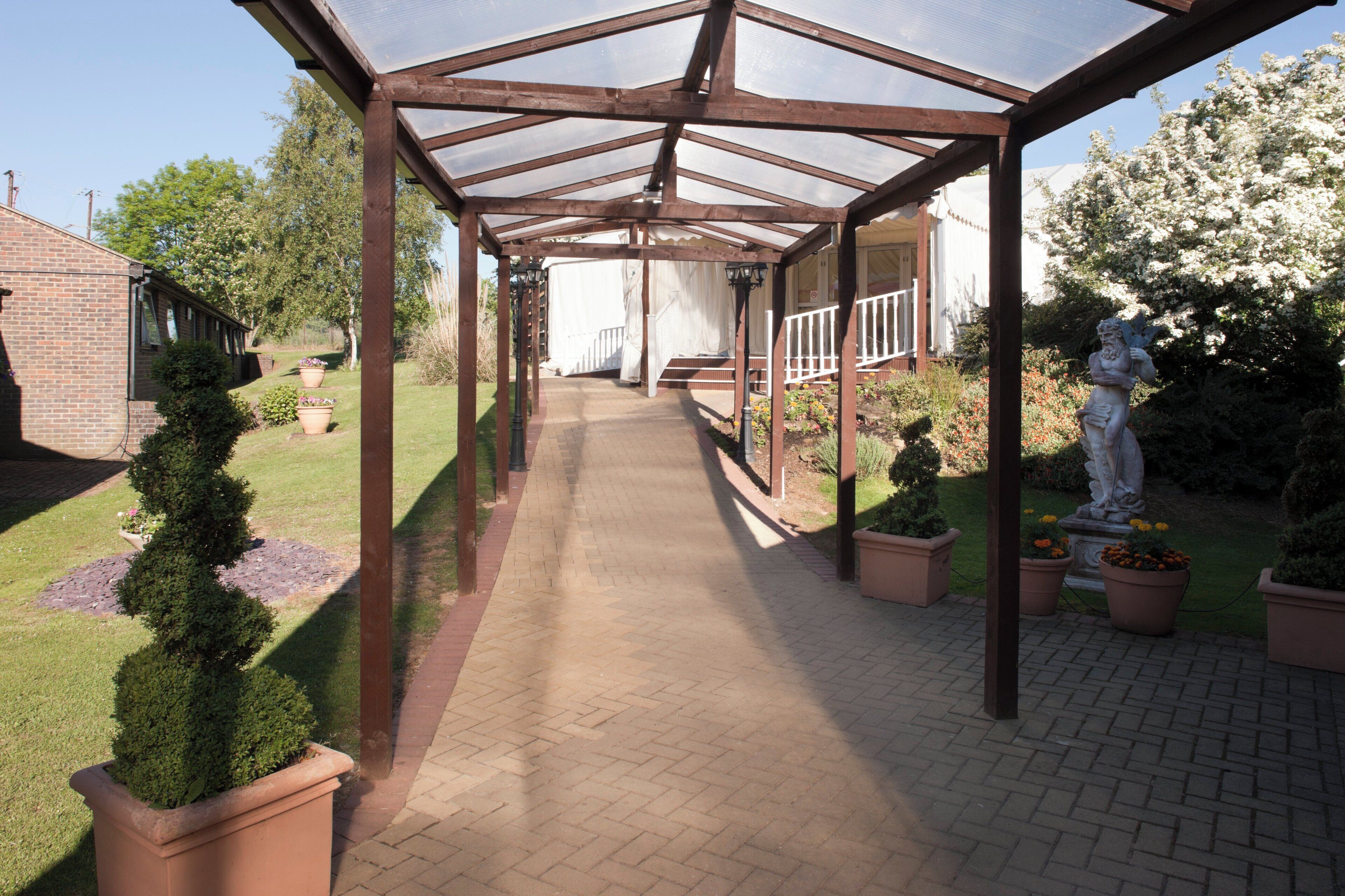 A covered walkway with a brick floor, flanked by potted plants and a statue.