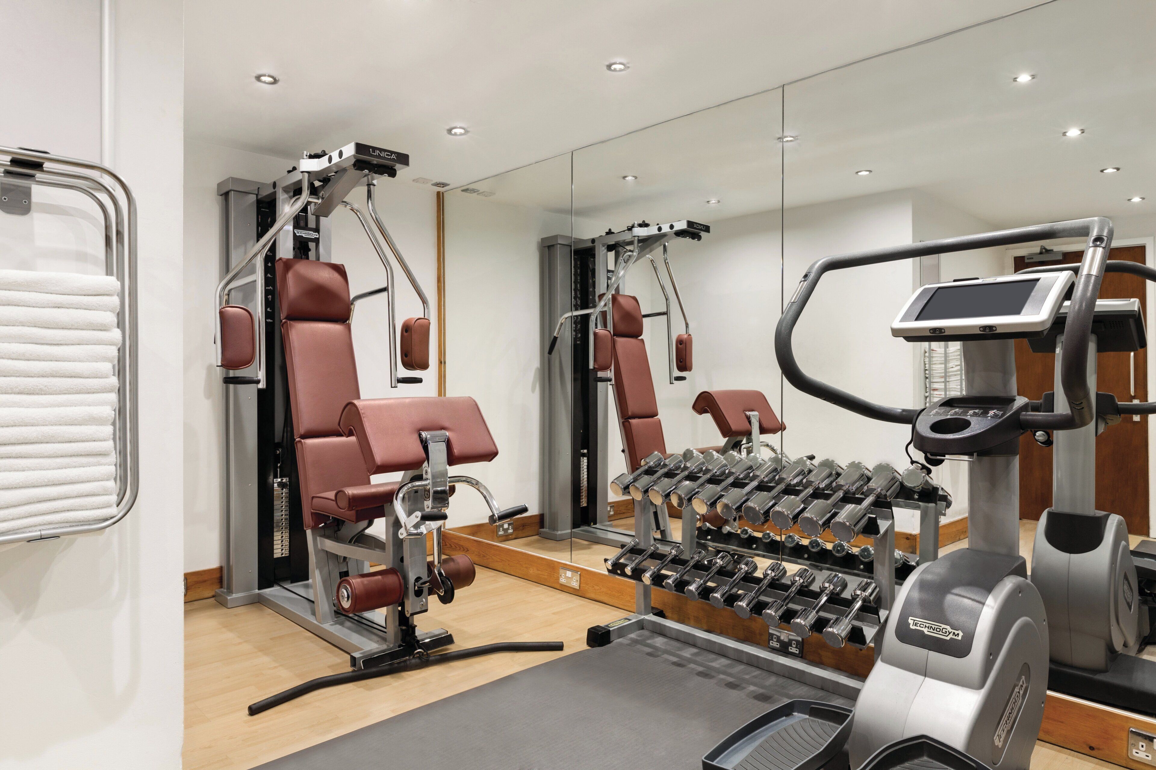 Un gimnasio moderno con equipo de ejercicio, espejos y una pantalla digital.