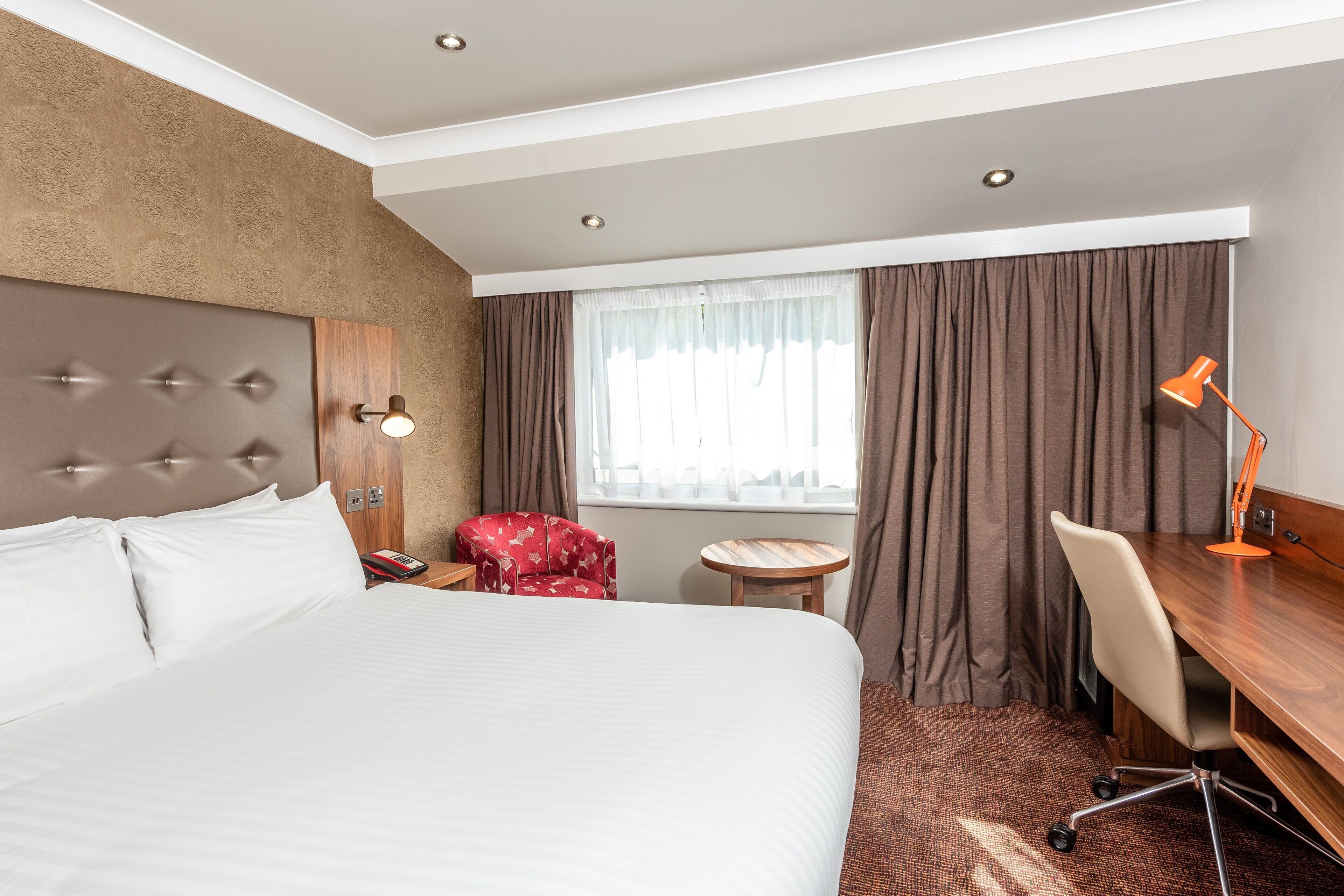 Una habitación de hotel con una cama grande, un escritorio, una silla, una mesita y una ventana con cortinas.
