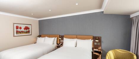 Habitación de hotel con dos camas, una mesita de noche, una lámpara, una silla y un cuadro en la pared.