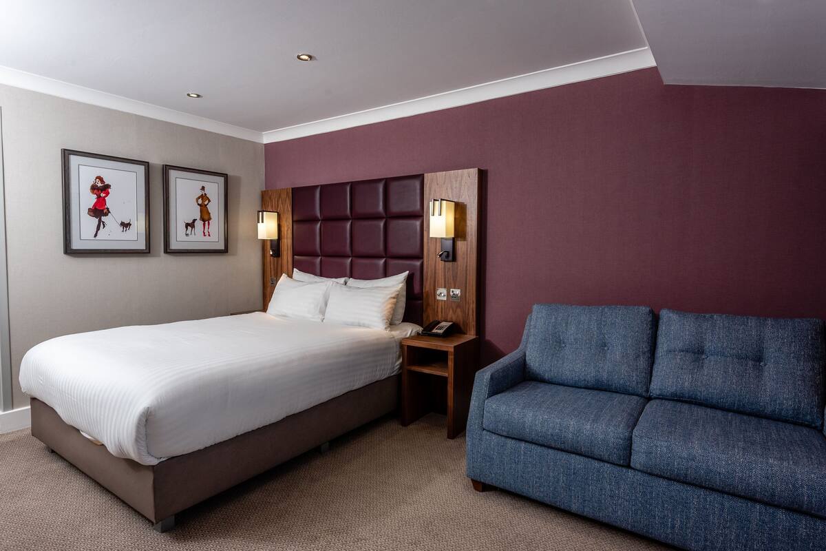 Een hotelkamer met een bed, een blauwe bank en twee foto's in lijsten aan de muur.