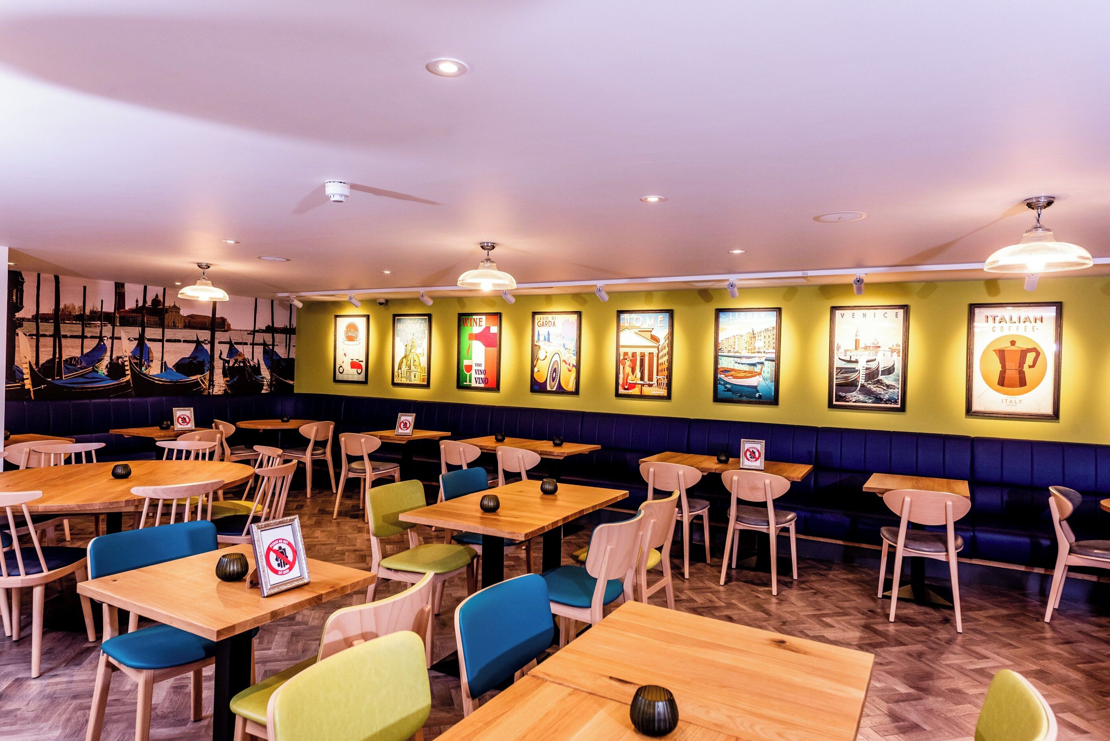 L’intérieur d’un restaurant présente de nombreuses tables et chaises, un mur orné de tableaux encadrés et un plafond doté d’un éclairage encastré.
