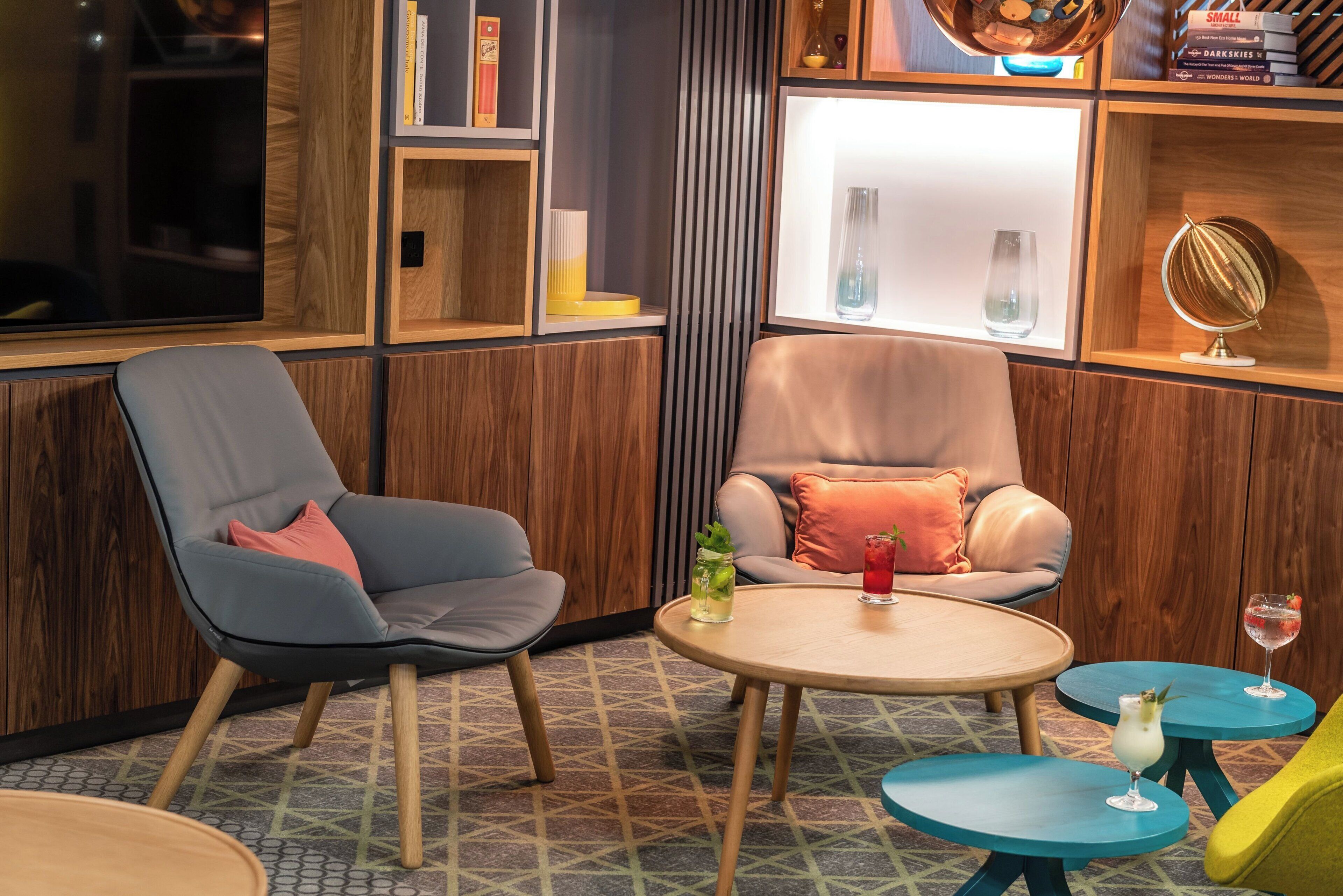 Un interior moderno con dos sillones, una mesita redonda y una estantería con libros y objetos decorativos.