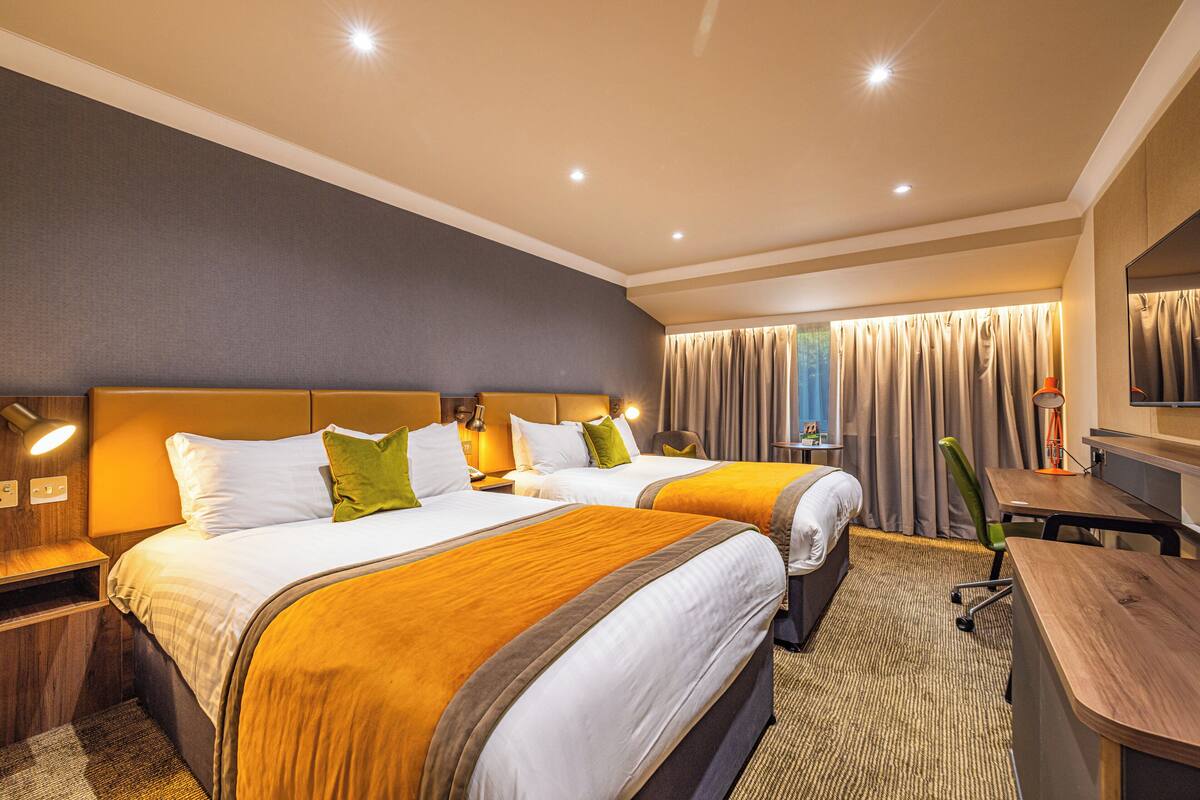 Hotelkamer met twee bedden, een bureau, een stoel, een televisie en een raam met gordijnen.