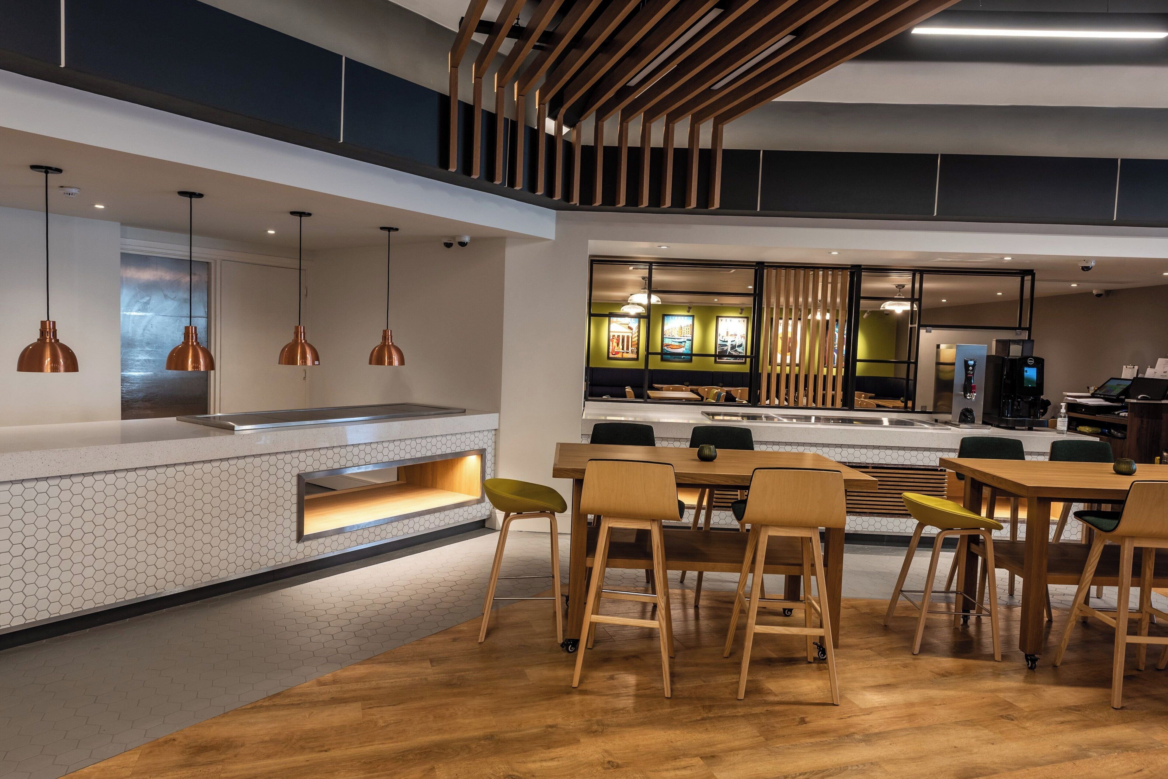 A modern restaurant interior with a long counter, pendant lighting, and a seating area with stools and tables.
