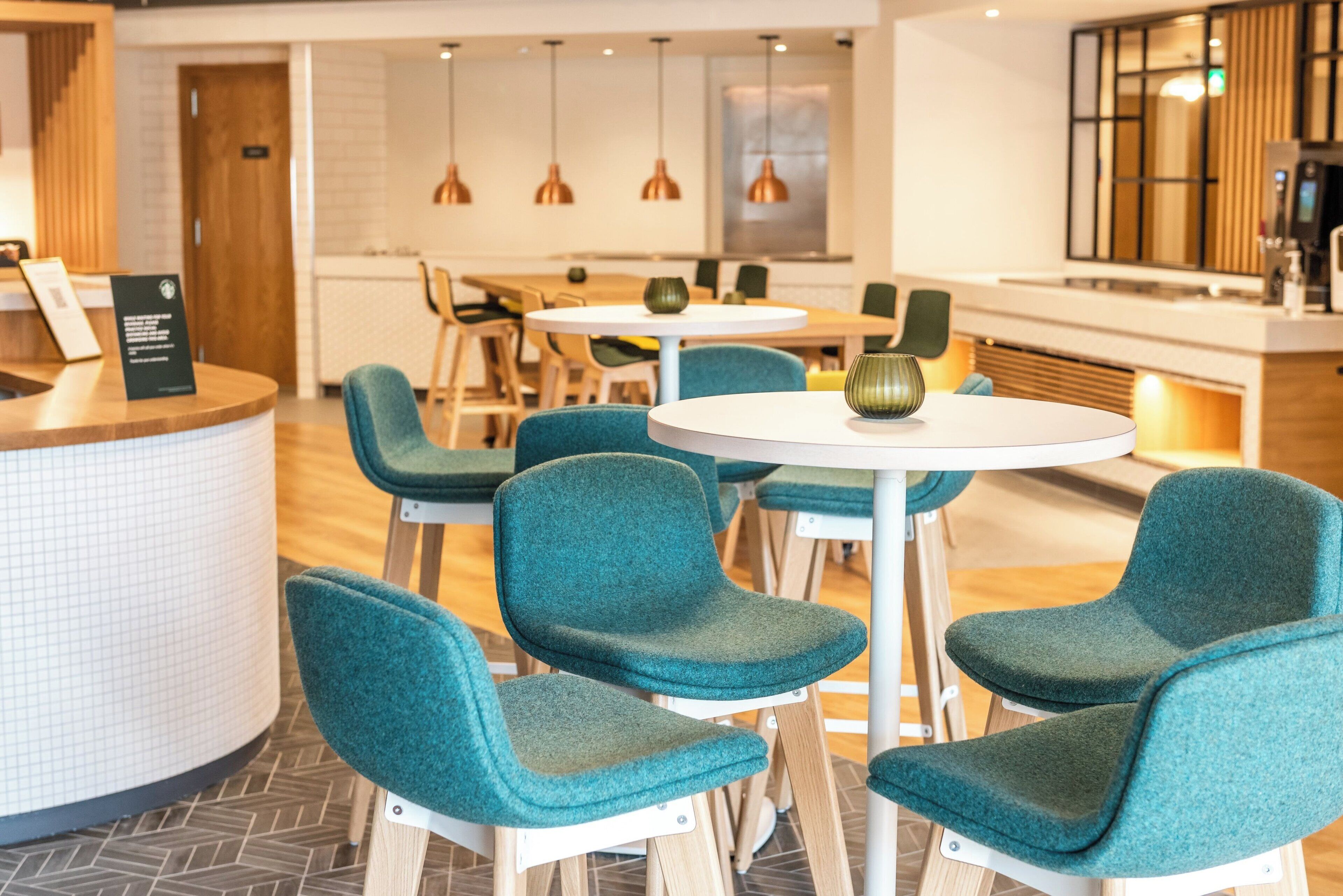 A modern restaurant interior with round tables, teal chairs, and pendant lighting.