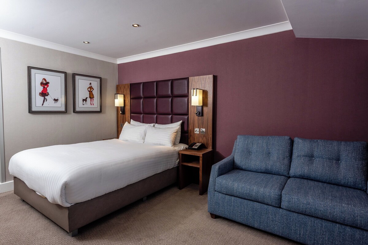 Une chambre d’hôtel avec un lit, une table de chevet, un canapé bleu et deux tableaux encadrés au mur.