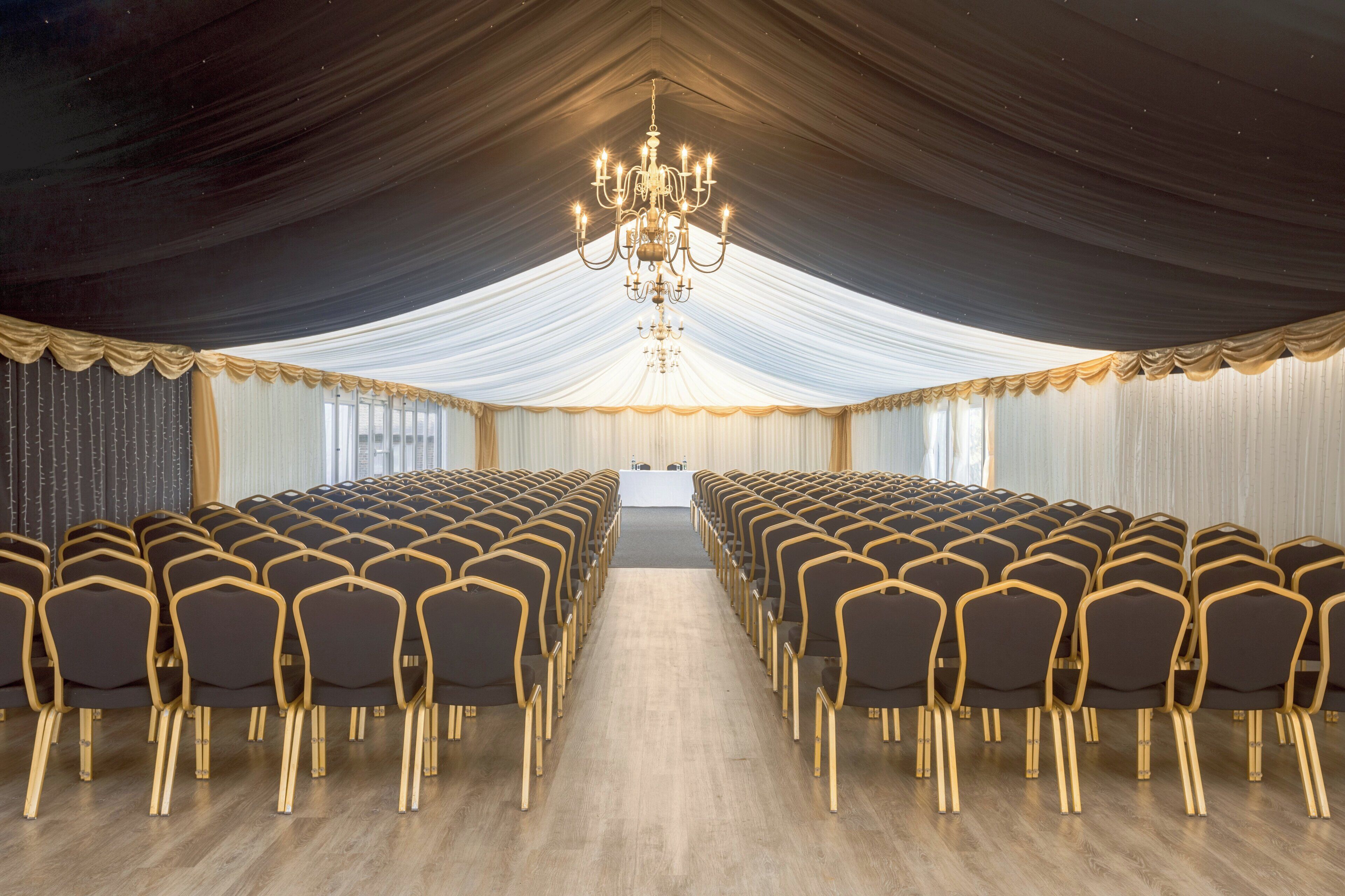 Une salle de conférence avec des rangées de chaises, un lustre et des rideaux tombants.
