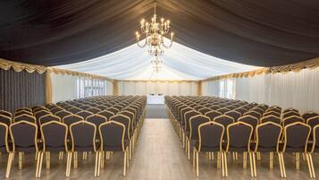 Une salle de conférence avec des rangées de chaises, un lustre et des rideaux tombants.