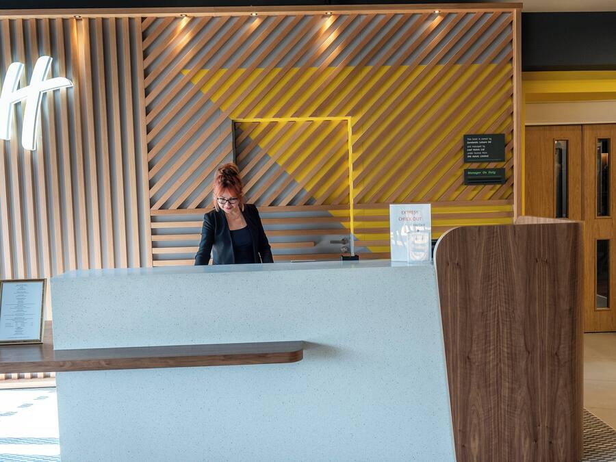 A reception desk with a modern design, featuring a wooden slat wall and a large illuminated 'H' sign.