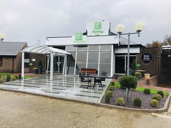 Un Holiday Inn con entrada cubierta, mesas al aire libre y un restaurante Bella Italia contiguo.