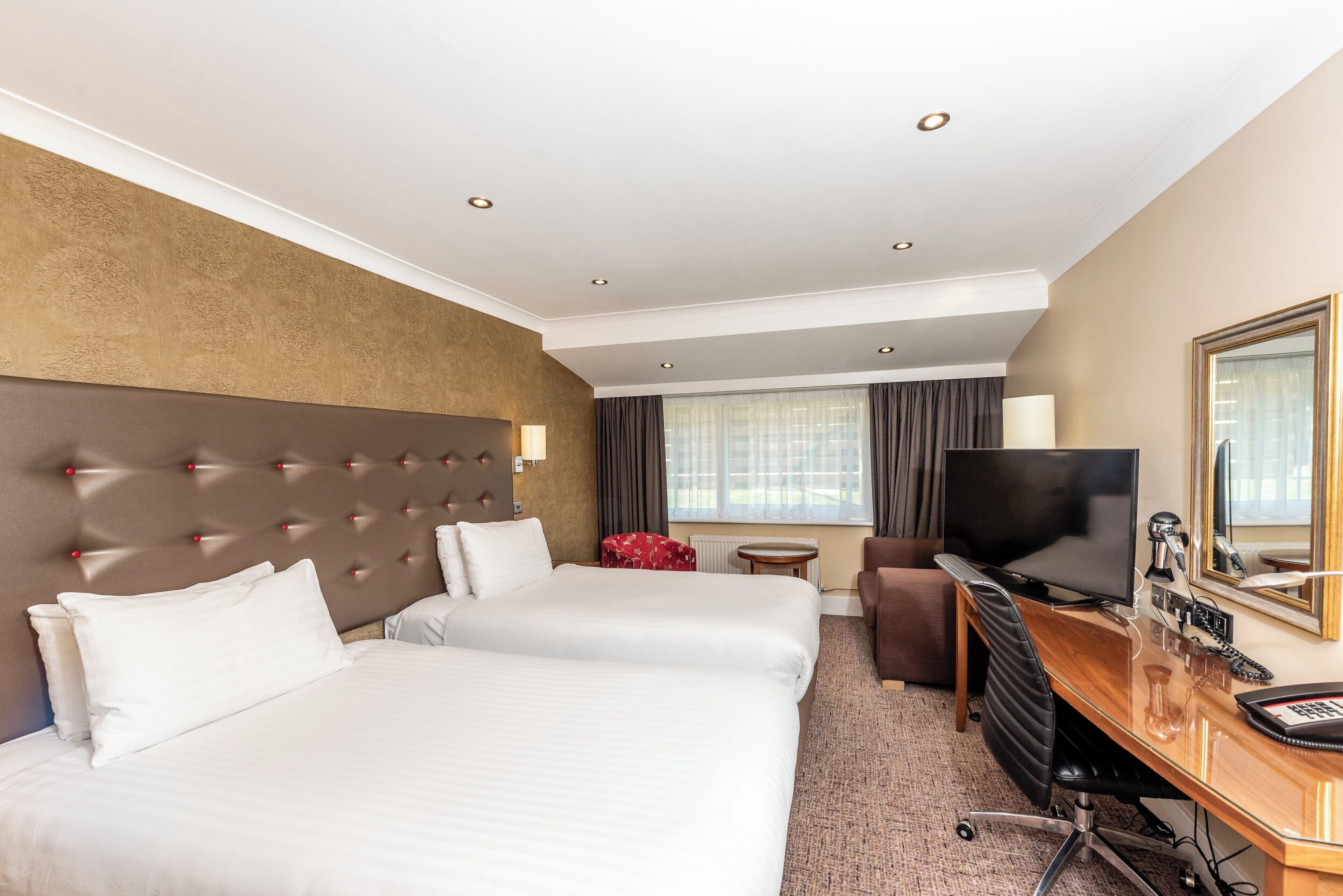 Una habitación de hotel con dos camas, un escritorio, un televisor y un espejo.