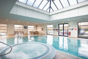 Une piscine intérieure avec un jacuzzi, des chaises en bois et une table.