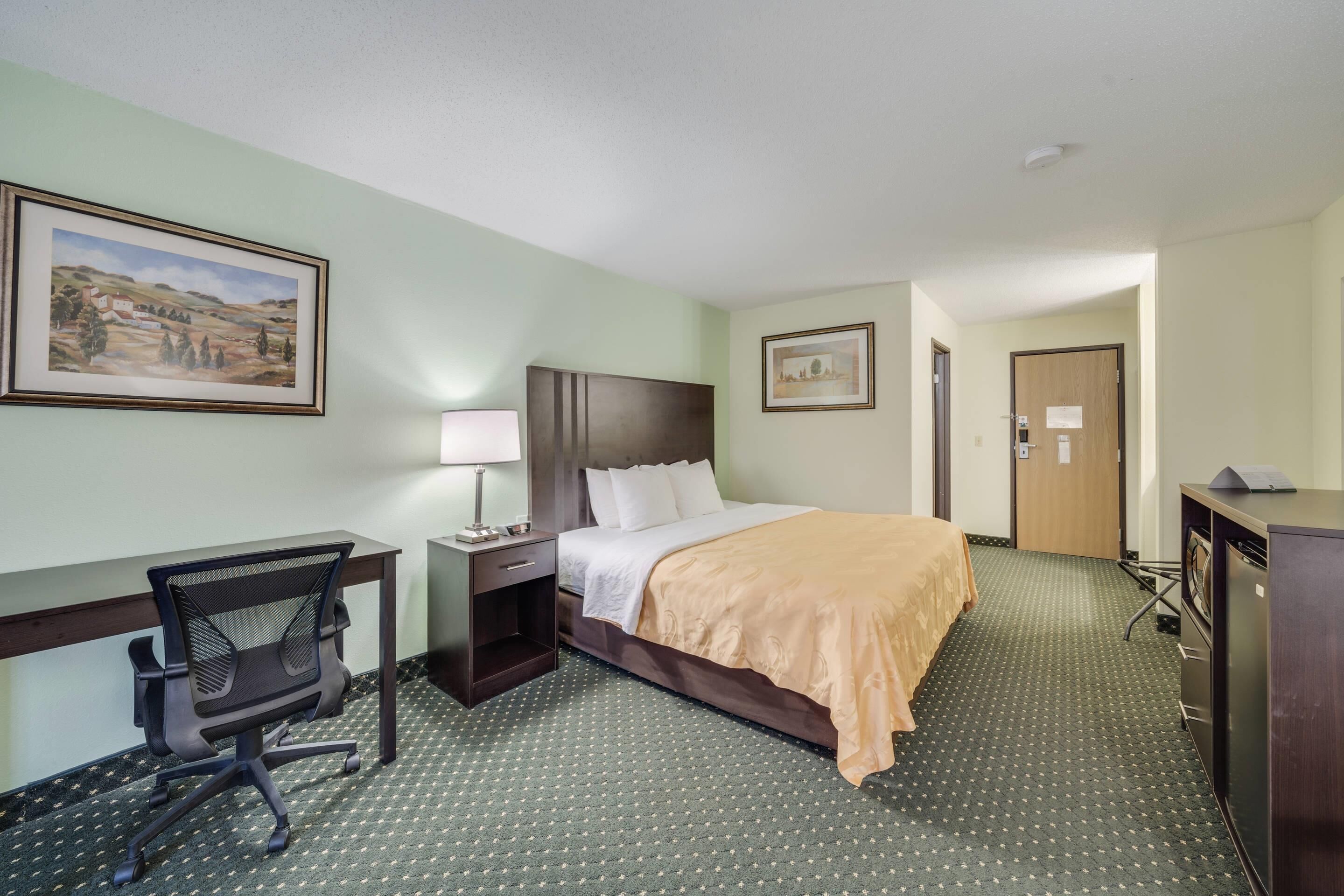 Habitación de hotel con cama, escritorio, silla y dos cuadros en las paredes.